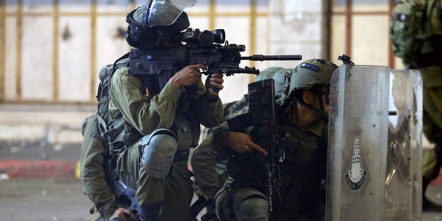 An Israeli soldier aims his weapon while others take cover behind their shields during a Palestinian protest amid a flare-up of Israeli-Palestinian violence, in Hebron in the Israeli-occupied West Bank May 11, 2021. 