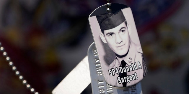 A relative of SP4 Donald Sargent wears his dog tags at the unveiling of a monument to honor the military passengers of Flying Tiger Line Flight 739, Saturday, May 15, 2021, in Columbia Falls, Maine. Sargent was among those killed on the secret mission to Vietnam in 1962. (Associated Press)