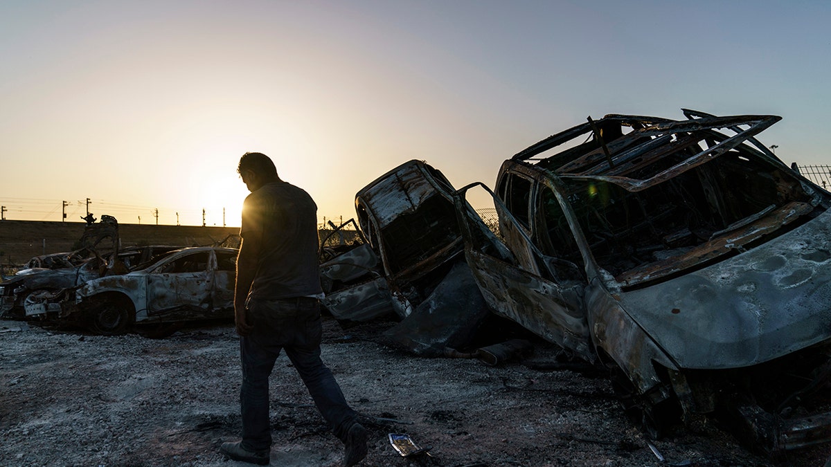 A worker passes torched cars piled up in a lot from clashes between Arabs, police, and Jews in the mixed Arab-Jewish town of Lod, central Israel, Tuesday, May 25, 2021. (AP Photo/David Goldman)