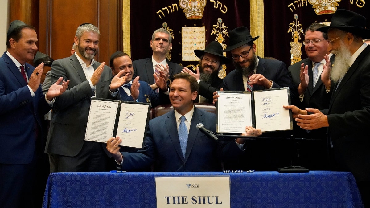 Surrounded by state legislators and Jewish leaders, Florida Gov. Ron DeSantis, center, holds up two bills that he signed, Monday, June 14, 2021. (AP Photo/Wilfredo Lee)