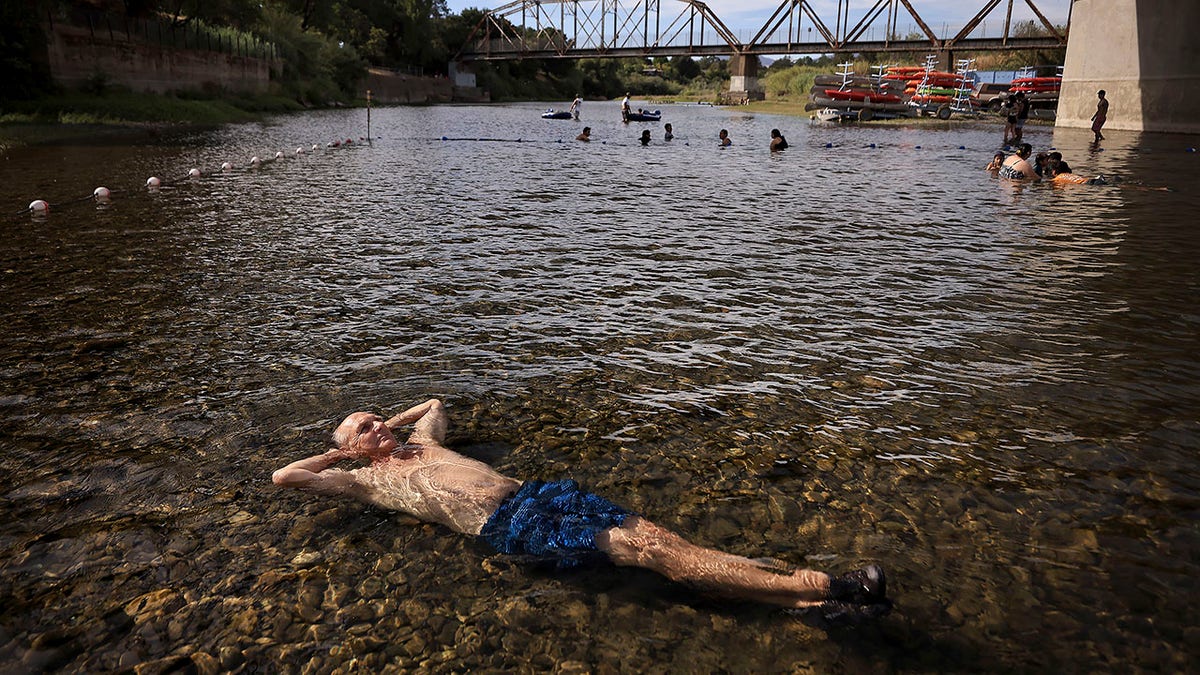 Gerry Huddleston of Santa Rosa, Calf. cools off in the very shallow water of the Russian River, Wednesday, June 16, 2021 at the Veterans Memorial Beach in Healdsburg, Calif. An unusually early and long-lasting heat wave brought more triple-digit temperatures Wednesday to a large swath of the U.S. West, raising concerns that such extreme weather could become the new normal amid a decades-long drought. (Kent Porter/The Press Democrat via AP)
