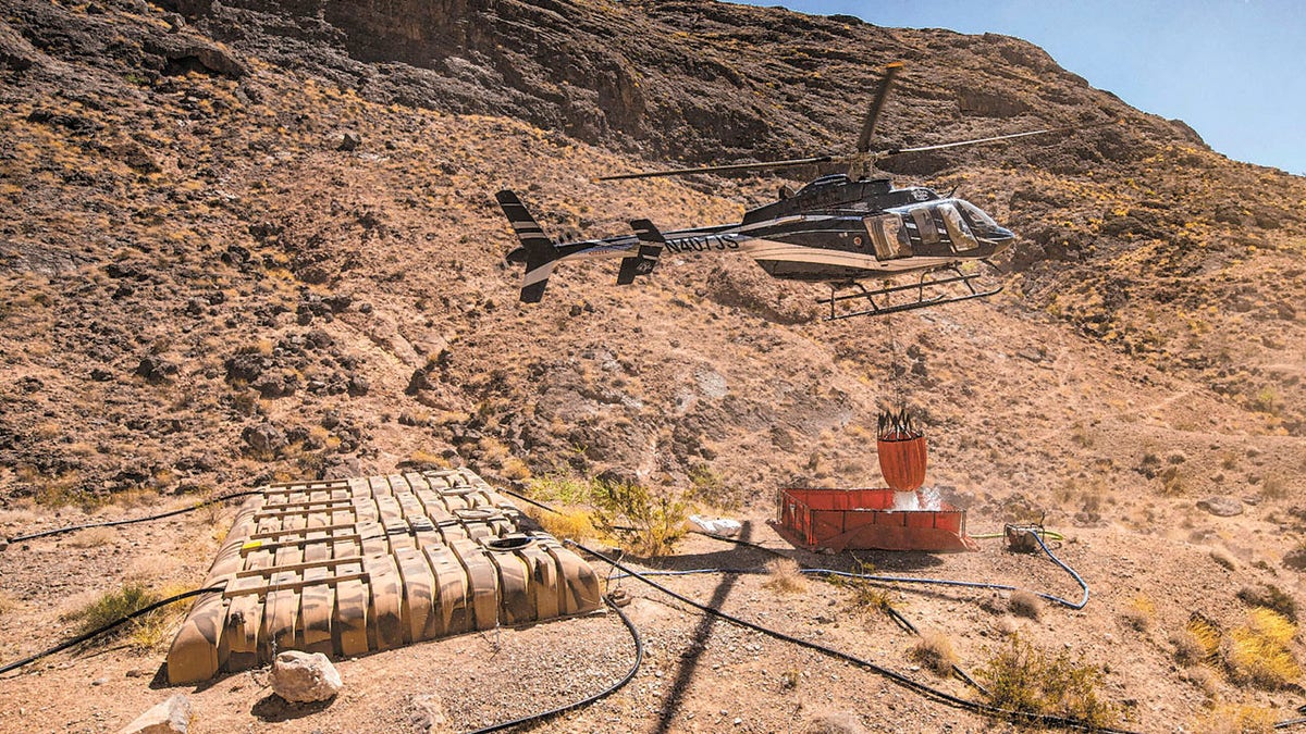 Rick Thielmann, chief pilot at the Nevada Department of Wildlife, releases water using a "Bambi Bucket" at the "flipper" guzzler in the Muddy Mountains, in Clark County, Nev., Tuesday, June 8, 2021, during an emergency water haul operation. While the guzzlers are primarily utilized to assist the bighorn sheep population in the area, they also provide water for a variety of animals that populate the area. (Chase Stevens/Las Vegas Review-Journal via AP)