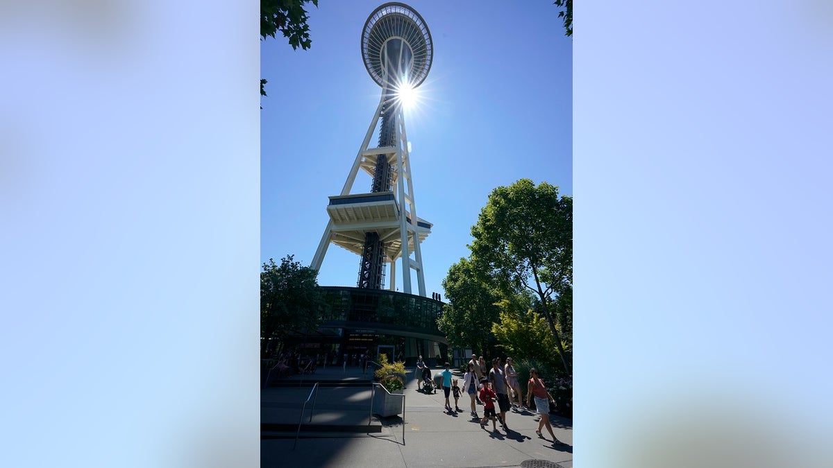 People walk as the sun shines behind the Space Needle, Monday in Seattle. Seattle and other cities broke all-time heat records over the weekend, with temperatures soaring well above 100 degrees. (AP Photo/Ted S. Warren)