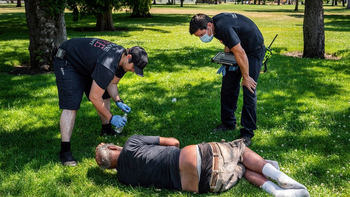 With the temperature well over 100 degrees, Spokane, Wash., firefighter Sean Condon, left and Lt. Gabe Mills, assigned to the Alternative Response Unit of of Station 1, check on the welfare of a man in Mission Park in Spokane, Wash., Tuesday, June 29, 2021. The special fire unit, which responds to low priority calls, has been kept busy during this week's heatwave. (Colin Mulvany/The Spokesman-Review via AP)