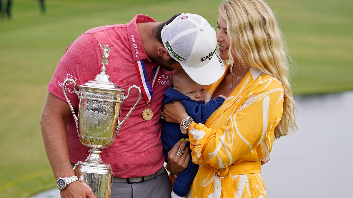 Jon Rahm, of Spain, holds the champions trophy for photographers as he stands with his wife, Kelley Rahm, and kisses their child, Kepa Rahm, 11 months, after the final round of the U.S. Open Golf Championship, Sunday, June 20, 2021, at Torrey Pines Golf Course in San Diego. (AP Photo/Marcio Jose Sanchez)