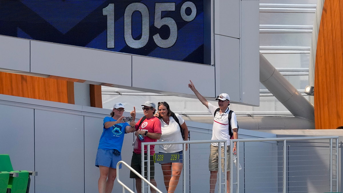 Fans pose for a picture near a sign displaying the current temperature at the U.S. Olympic Track and Field Trials Sunday, June 27, 2021, in Eugene, Ore. Events were postponed until later in the day due to high heat. (AP Photo/Charlie Riedel)