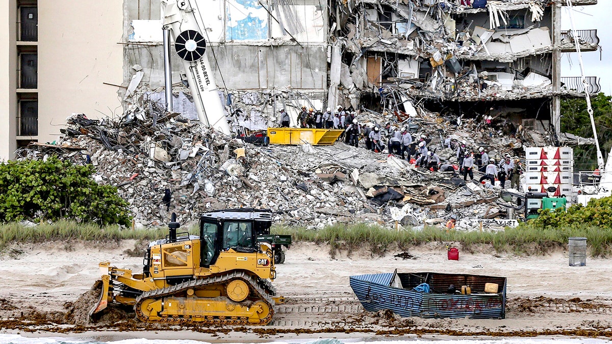 A bulldozer pulls a possible migrant boat that washed ashore in Surfside, Fla., as search and rescue teams look for survivors at the collapsed 12-story oceanfront condo, Champlain Towers South, Tuesday, June 29, 2021. (Al Diaz/Miami Herald via AP)