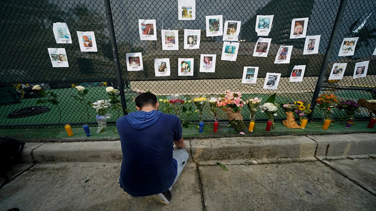 Leo Soto, who created this memorial with grocery stores donating flowers and candles, pauses in front of photos of some of the missing people that he put on a fence, near the site of the disaster in Surfside, Fla., on Friday. (AP)