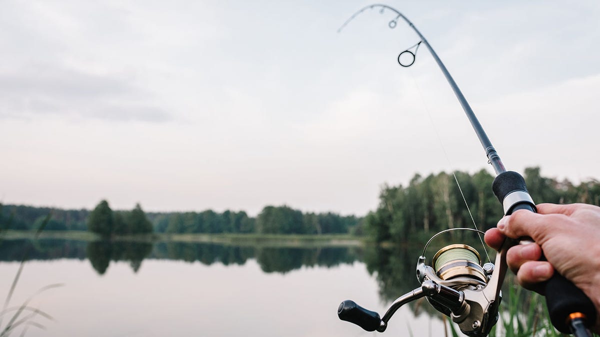 Fisherman with rod, spinning reel on the river bank. Fishing for pike, perch, carp. Fog against the backdrop of lake. background Misty morning. wild nature. Article about fishing day.