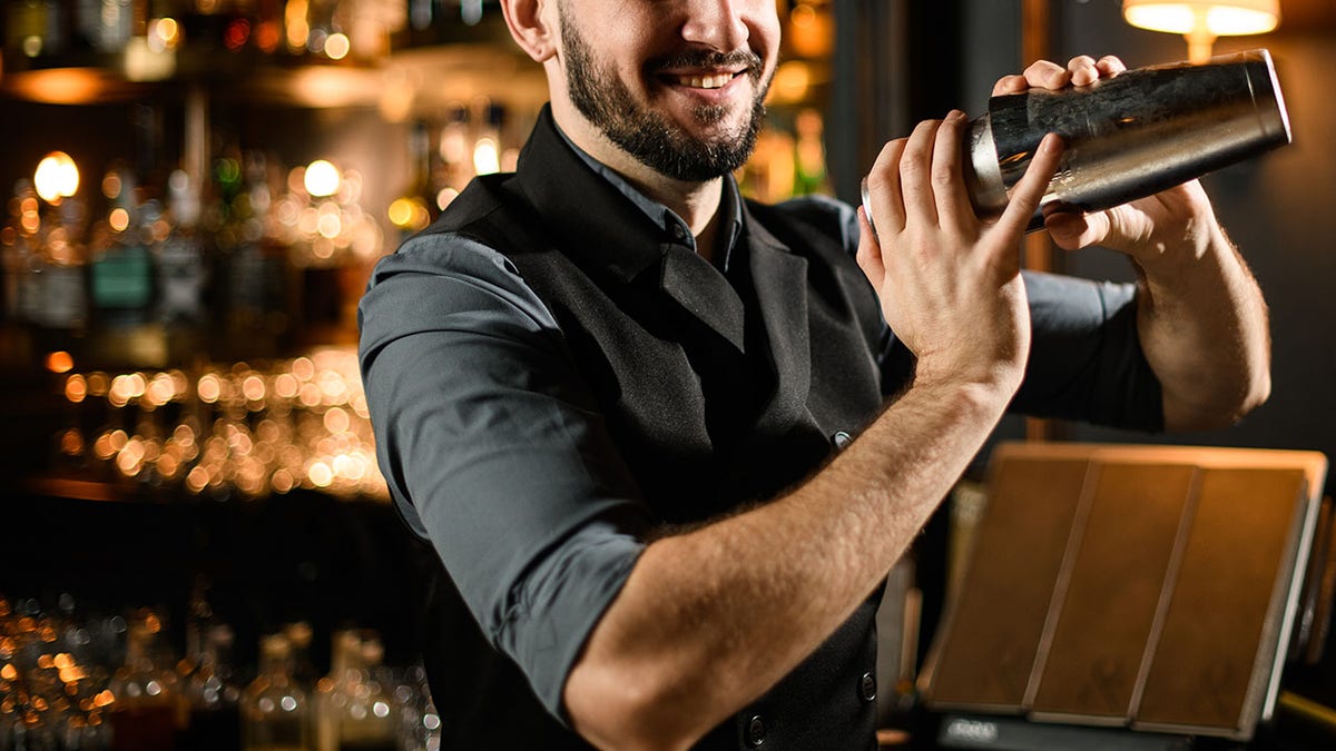 Male bartender shakes cocktail in stainless steel shaker