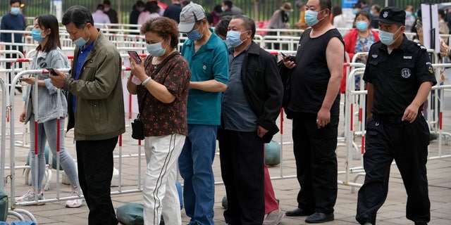 A security guard watches residents wearing face masks to help curb the spread of the coronavirus line up to receive the Sinopharm COVID-19 vaccine at a vaccination center in the Central Business District in Beijing, Wednesday, June 2, 2021. After a slow start, China is now doing what virtually no other country in the world can: harnessing the power and all-encompassing reach of its one-party system and a maturing domestic vaccine industry to administer shots at a staggering pace. (AP Photo/Andy Wong)