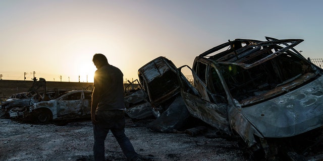 A worker passes torched cars piled up in a lot from clashes between Arabs, police, and Jews in the mixed Arab-Jewish town of Lod, central Israel, Tuesday, May 25, 2021.  (AP Photo/David Goldman)