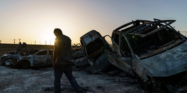 A worker passes torched cars piled up in a lot from clashes between Arabs, police, and Jews in the mixed Arab-Jewish town of Lod, central Israel, Tuesday, May 25, 2021. (AP Photo/David Goldman)