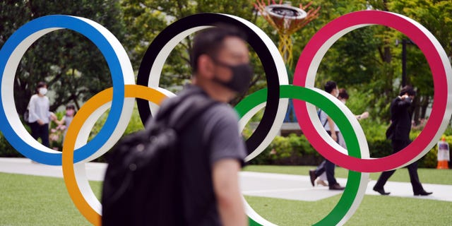 People walk near the Olympic Rings Wednesday, June 2, 2021, in Tokyo. Roads are being closed off around Tokyo Olympic venues including the new $1.4 billion National Stadium where the opening ceremony is set for July 23. (AP Photo/Eugene Hoshiko)