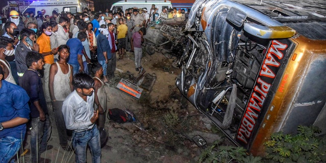 Onlookers gather near the wreckage after a bus carrying migrant workers after the lifting of coronavirus restrictions hit a delivery van on a highway near Kanpur, Uttar Pradesh state, India, Tuesday, June 8, 2021. (AP Photo)