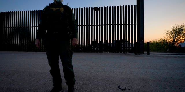 In this March 21, 2021 file photo, a U.S. Customs and Border Protection agent looks on near a gate on the U.S.-Mexico border wall as agents take migrants into custody, in Abram-Perezville, Texas. (AP Photo/Julio Cortez, File)