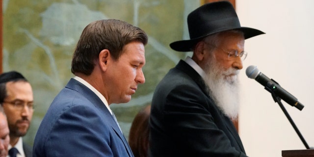 Florida Gov. Ron DeSantis, left, and Rabbi Sholom Lipskar participate in a moment of silence, Monday, June 14, 2021, at the Shul of Bal Harbour, a Jewish community center in Surfside, Fla. (AP Photo/Wilfredo Lee)