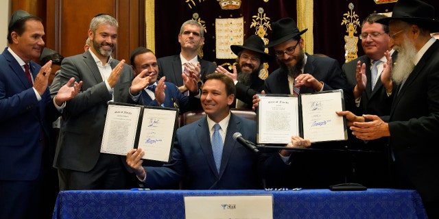 Surrounded by state legislators and Jewish leaders, Florida Gov. Ron DeSantis, center, holds up two bills that he signed, Monday, June 14, 2021. (AP Photo/Wilfredo Lee)