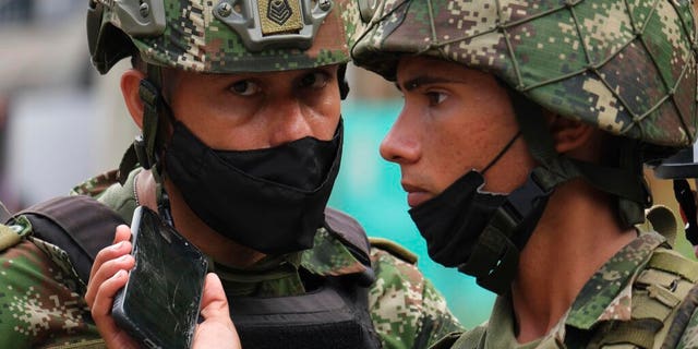 Soldiers listen to the news on a mobile phone near the military base where a car bomb exploded in Cucuta, Colombia, Tuesday, June 15, 2021.