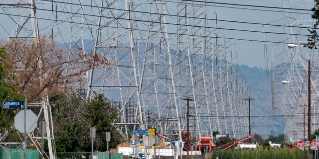 In this Aug. 15, 2020 file photo an automobile drives down a road as radiant heat is seen coming off of the pavement near high tension electrical lines in the North Hollywood section of Los Angeles. 