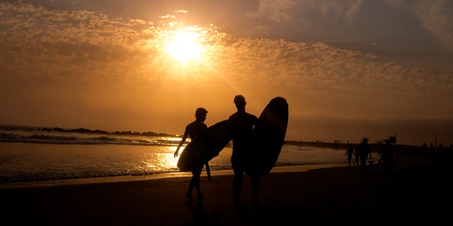 Surfers are silhouetted as they leave the water during the sun set on Wednesday, June 16, 2021, in the Venice Beach section of Los Angeles. An unusually early and long-lasting heat wave brought more triple-digit temperatures Wednesday to a large swath of the U.S. West, raising concerns that such extreme weather could become the new normal amid a decades-long drought.(AP Photo/Ringo H.W. Chiu)