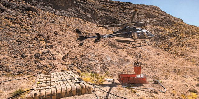 Rick Thielmann, chief pilot at the Nevada Department of Wildlife, releases water using a "Bambi Bucket" at the "flipper" guzzler in the Muddy Mountains, in Clark County, Nev., Tuesday, June 8, 2021, during an emergency water haul operation. While the guzzlers are primarily utilized to assist the bighorn sheep population in the area, they also provide water for a variety of animals that populate the area. (Chase Stevens/Las Vegas Review-Journal via AP)