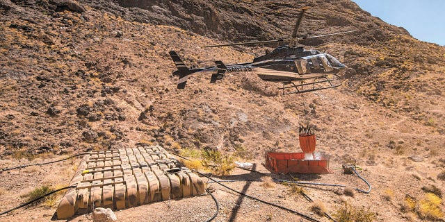 Rick Thielmann, chief pilot at the Nevada Department of Wildlife, releases water using a "Bambi Bucket" at the "flipper" guzzler in the Muddy Mountains, in Clark County, Nev., Tuesday, June 8, 2021, during an emergency water haul operation. While the guzzlers are primarily utilized to assist the bighorn sheep population in the area, they also provide water for a variety of animals that populate the area. (Chase Stevens/Las Vegas Review-Journal via AP)