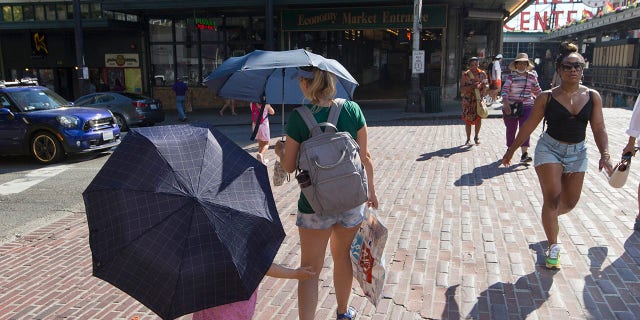 Sabina Ehmann and her daughter Vivian, visiting Seattle from North Carolina, are prepared with umbrellas to shield the sun during a heat wave hitting the Pacific Northwest, Sunday, June 27, 2021, in Seattle. (AP Photo/John Froschauer)