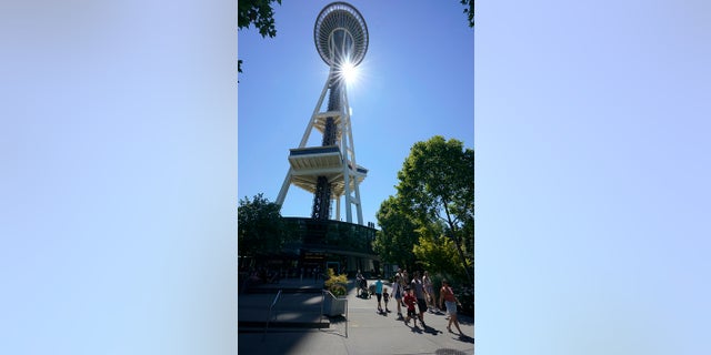 People walk as the sun shines behind the Space Needle, Monday in Seattle. Seattle and other cities broke all-time heat records over the weekend, with temperatures soaring well above 100 degrees. (AP Photo/Ted S. Warren)