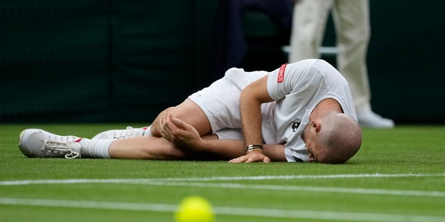 Adrian Mannarino of France lies on the ground in pain during the men's singles first-round match against Switzerland's Roger Federer on day two of the Wimbledon Tennis Championships in London, Tuesday June 29, 2021. (AP Photo/Kirsty Wigglesworth)