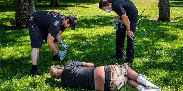 With the temperature well over 100 degrees, Spokane, Wash., firefighter Sean Condon, left and Lt. Gabe Mills, assigned to the Alternative Response Unit of of Station 1, check on the welfare of a man in Mission Park in Spokane, Wash., Tuesday, June 29, 2021. The special fire unit, which responds to low priority calls, has been kept busy during this week's heatwave. (Colin Mulvany/The Spokesman-Review via AP)