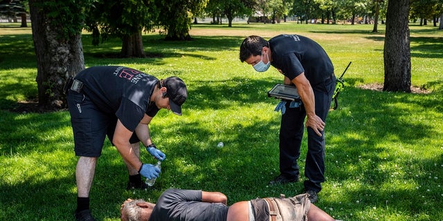 With the temperature well over 100 degrees, Spokane, Wash., firefighter Sean Condon, left and Lt. Gabe Mills, assigned to the Alternative Response Unit of of Station 1, check on the welfare of a man in Mission Park in Spokane, Wash., Tuesday, June 29, 2021. The special fire unit, which responds to low priority calls, has been kept busy during this week's heatwave. (Colin Mulvany/The Spokesman-Review via AP)