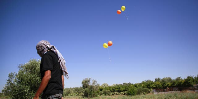 Masked Palestinian man walks away after launching incendiary balloons towards Israel.  (Ahmed Zakot / SOPA Images/Sipa USA)(Sipa via AP Images)