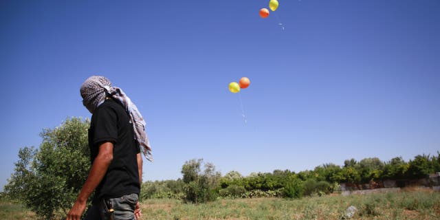 Masked Palestinian man walks away after launching incendiary balloons towards Israel.  (Ahmed Zakot / SOPA Images/Sipa USA)(Sipa via AP Images)