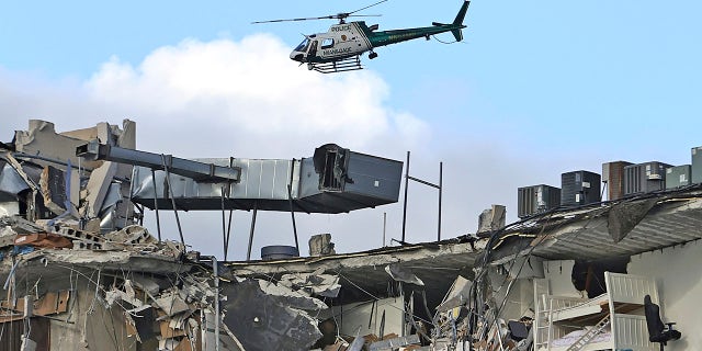 A Miami-Dade Police helicopter flies over the Champlain Towers South Condo after the multistory building partially collapsed, Thursday, June 24, 2021, in Surfside, Florida. 