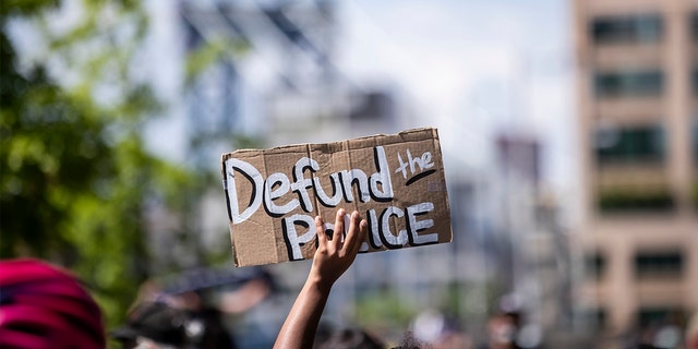 A protester holds up a homemade sign that says, "Defund the Police" with the Manhattan Bridge behind them as they perform a peaceful protest walk across the Brooklyn Bridge. (Photo by Ira L. Black/Corbis via Getty Images)