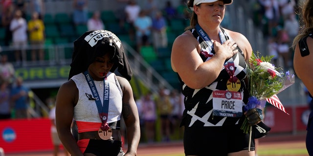Gwendolyn Berry, left, drapes her Activist Athlete T-Shirt over her head as DeAnna Price stands for the national anthem after the finals of the women's hammer throw at the U.S. Olympic Track and Field Trials Saturday, June 26, 2021, in Eugene, Ore. Price won and Berry finished third. (AP Photo/Charlie Riedel)