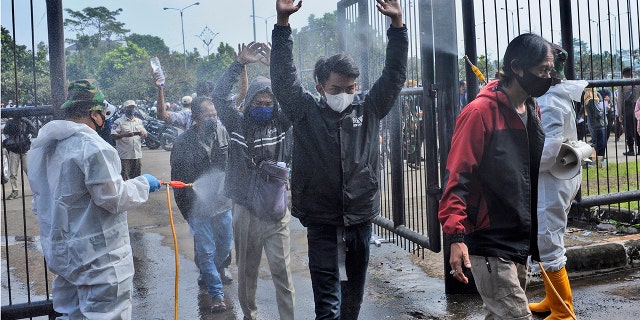 June 17, 2021: Soldiers in protective suits spray disinfectant on people entering the Gelora Bandung Lautan Api Stadium to receive the Sinovac COVID-19 vaccine during a mass vaccination in Bandung, West Java, Indonesia.