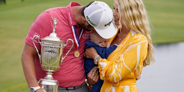 Jon Rahm, of Spain, holds the champions trophy for photographers as he stands with his wife, Kelley Rahm, and kisses their child, Kepa Rahm, 11 months, after the final round of the U.S. Open Golf Championship, Sunday, June 20, 2021, at Torrey Pines Golf Course in San Diego. (AP Photo/Marcio Jose Sanchez)