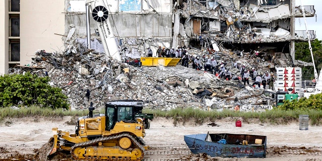 A bulldozer pulls a possible migrant boat that washed ashore in Surfside, Fla., as search and rescue teams look for survivors at the collapsed 12-story oceanfront condo, Champlain Towers South, Tuesday, June 29, 2021. (Al Diaz/Miami Herald via AP)