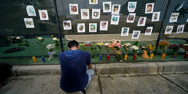 Leo Soto, who created this memorial with grocery stores donating flowers and candles, pauses in front of photos of some of the missing people that he put on a fence, near the site of the disaster in Surfside, Fla., on Friday. (AP)