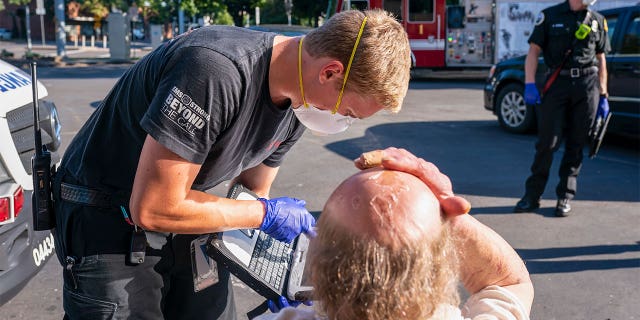 A paramedic with Falck Northwest ambulances treats a man experiencing heat exposure during a heat wave, Saturday, June 26, 2021, in Salem, Oregon. (AP Photo/Nathan Howard)