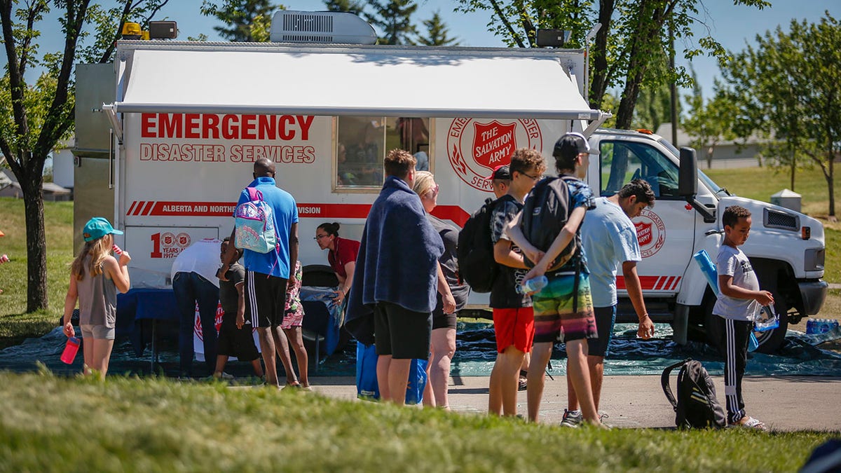A Salvation Army EMS vehicle is setup as a cooling station as people lineup to get into a splash park while trying to beat the heat in Calgary, Alberta, Wednesday, June 30, 2021. (Jeff McIntosh/The Canadian Press via AP)
