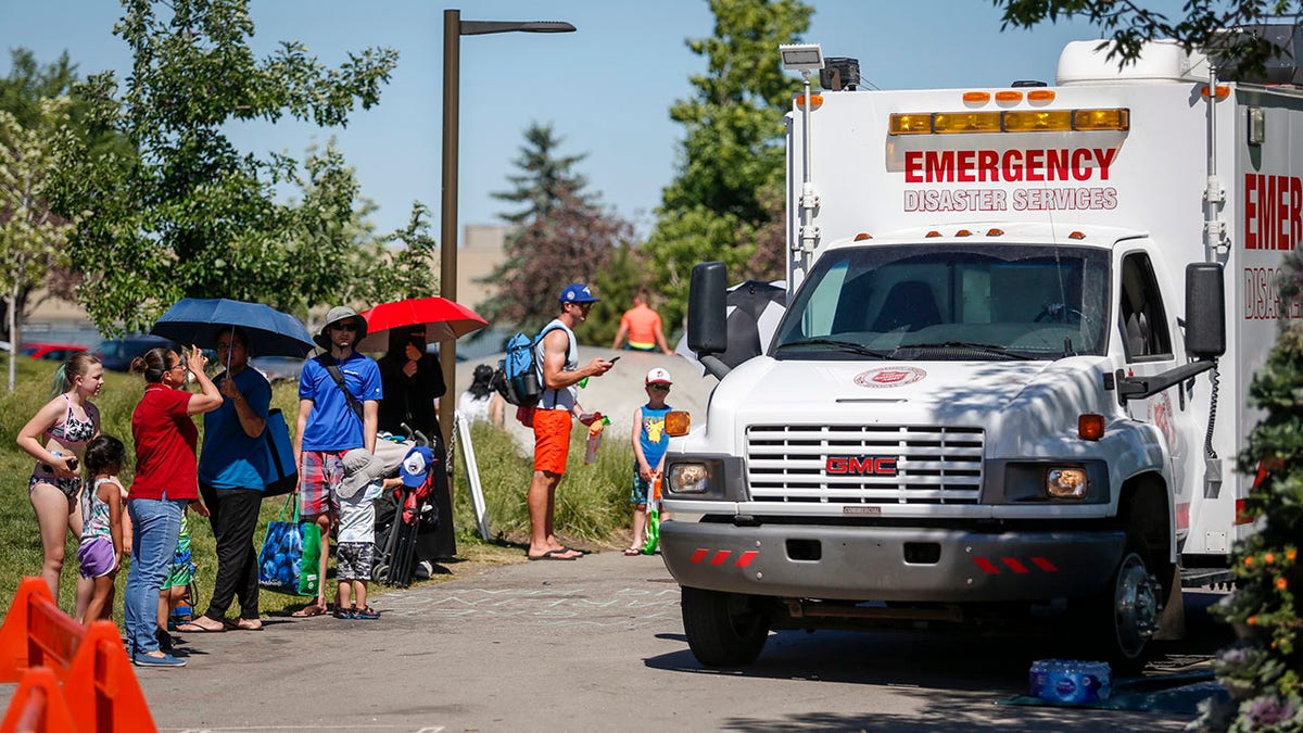 A Salvation Army EMS vehicle is setup as a cooling station as people lineup to get into a splash park while trying to beat the heat in Calgary, Alberta., Wednesday, June 30, 2021.