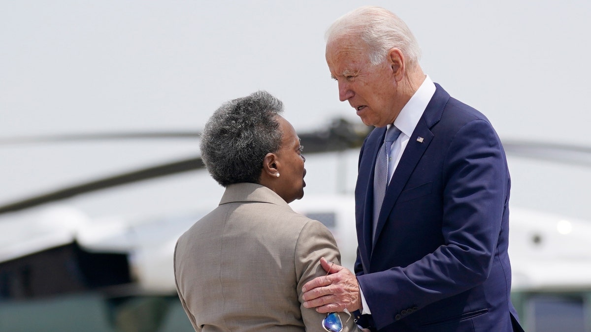 President Joe Biden in a blue suit greets Chicago Mayor Lori Lightfoot in a tan suit with a helicopter in the background