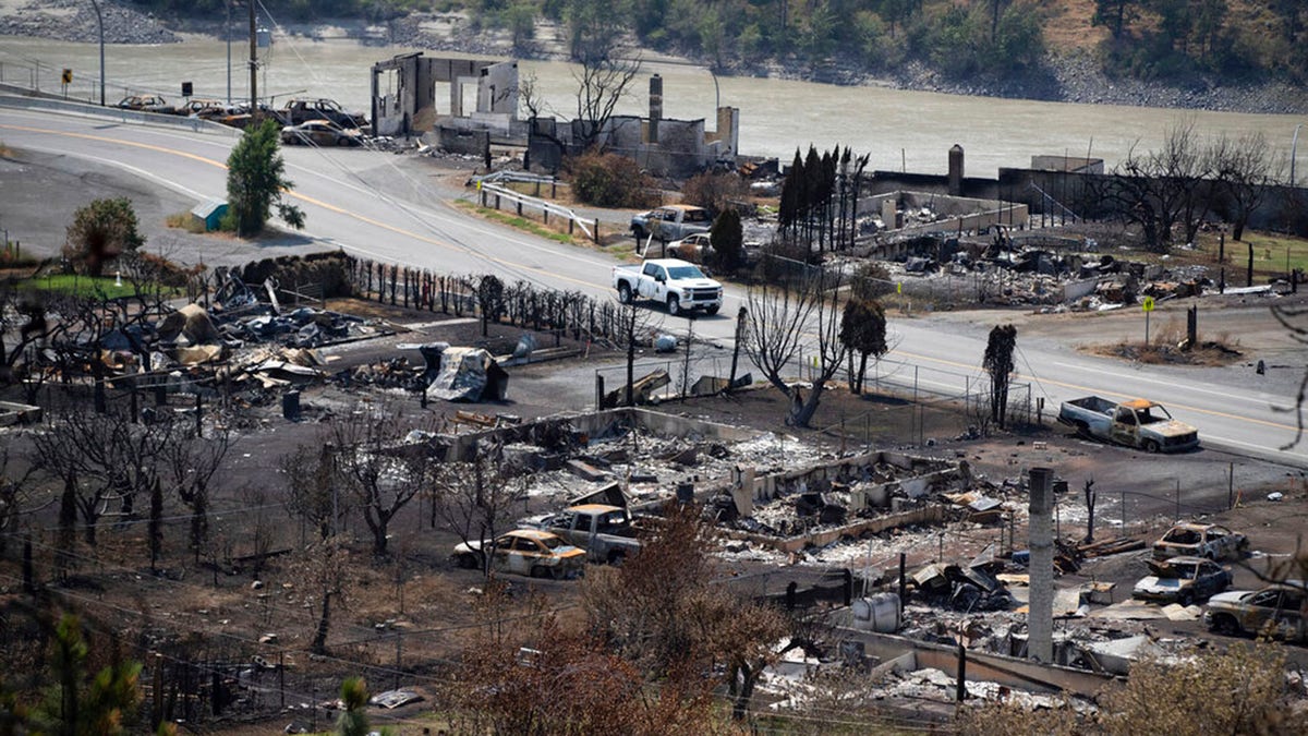 A Royal Canadian Mounted Police (RCMP) vehicle drives past the remains of vehicles and structures in Lytton, British Columbia, Friday, July 9, 2021, after a wildfire destroyed most of the village on June 30. (Darryl Dyck/The Canadian Press via AP)