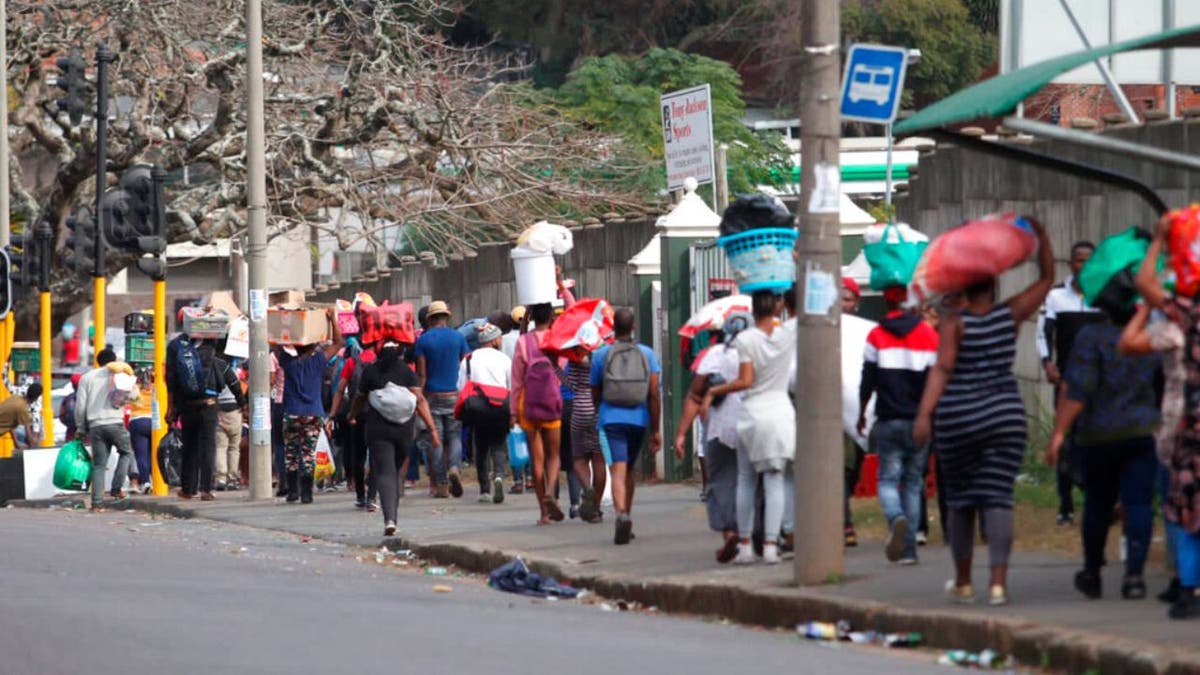 People make their way from a shopping mall carrying goods in Durban, South Africa, Tuesday July 13, 2021, as the looting and violence continue. 