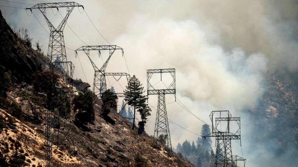 Smoke billows behind power lines as the Dixie Fire burns along Highway 70 in Plumas National Forest, Calif., on Friday, July 16, 2021.