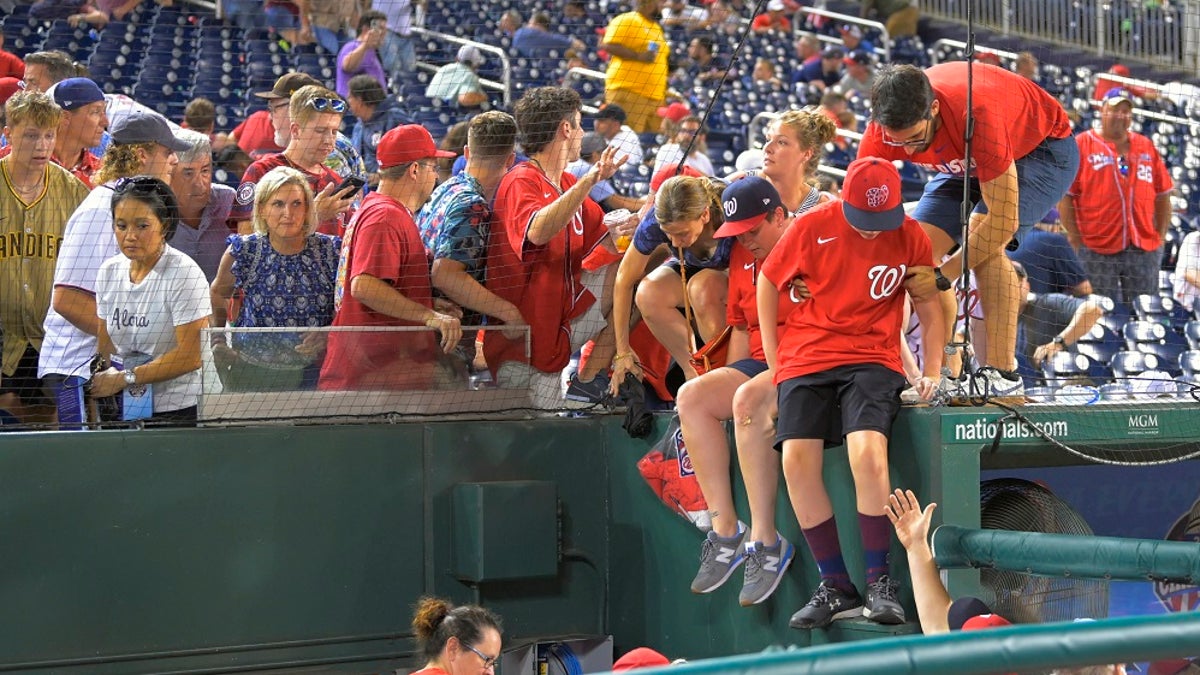 Fans jump into a camera well after hearing gunfire from outside Nationals Park during a Saturday baseball game between the San Diego Padres and the Washington Nationals. (John McDonnell/The Washington Post via AP)