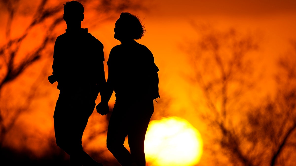 A couple walks through a park at sunset in Kansas City, Mo on March 10, 2021. (AP Photo/Charlie Riedel, File)